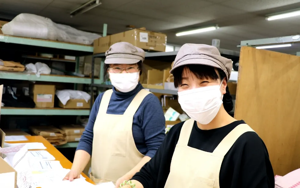 ヘルメットや作業着を着た工場のチームメンバーが、笑顔で肩を組みながらカメラに向かってポーズを取っている。